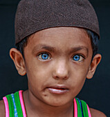 Mirsharai, Bangladesh - 20 September 2020: View of a young boy's captivating, piercing blue eyes contrasting with his warm skin tone and dark cap.