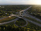Aerial view of the intricate highway interchange weaving through a tapestry of lush green trees under the soft glow of the setting sun, Charlotte, North Carolina, United States.