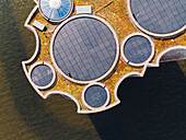 Luftaufnahme einer schwimmenden, scheibenförmigen Struktur mit Solarzellen und grüner Vegetation, die sich vom dunklen Wasser abhebt, Vejle, Dänemark.