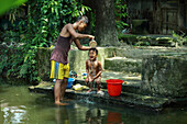 Mirsharai, Bangladesh - 20 September 2019: View of a vibrant scene where a person pours water over a child near lush greenery, creating a moment of refreshing contrast against the rustic stone steps.