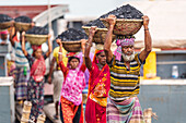 Dhaka, Bangladesh - 14 May 2023: View of laborers carrying heavy baskets of coal on their heads, a stark contrast of labor against a backdrop of muted tones.
