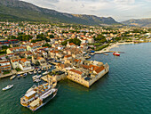 Luftaufnahme von sonnenverwöhnten Steingebäuden mit Terrakotta-Dächern an der türkisfarbenen Adria in der Nähe der Festung Kastilac, einer lebhaften Küstenszene, Kastel Gomilica, Gespanschaft Split-Dalmatien, Kroatien.