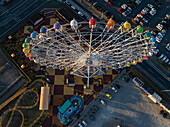 Luftaufnahme eines bunten Riesenrads und einer Miniatur-Achterbahn im Kontrast zum schachbrettartigen Boden und den geparkten Autos, Osaka, Japan.