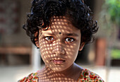 Rangpur, Bangladesh - 30 November 2019: View of a young girl's intense gaze, her face adorned with a lattice of shadow, highlighting the innocence and mystery.