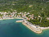 Luftaufnahme des lebhaften Küstendorfs zwischen der türkisfarbenen Adria und den üppig grünen Bergen, Igrane, Gespanschaft Split-Dalmatien, Kroatien.