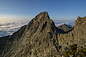 Aerial view of Maly Ladovy Stit piercing through a sea of clouds, its rocky facade bathed in the soft glow of the morning sun, Tatranská Javorina, Prešov Region, Slovakia.