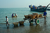 Cox's Bazar, Bangladesh - 07 March 2022: View of fishermen hauling their catch ashore, contrasting the dark, weathered wood of the fishing boat with the bright, woven texture of the baskets.