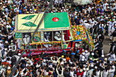 Chattogram, Bangladesh - 08 October 2022: Aerial view of a decorated vehicle adorned with flags and flowers, surrounded by a dense crowd of people in the city streets.