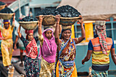 Dhaka, Bangladesh - 14 May 2023: View of women carrying baskets of coal on their heads, their vibrant saris contrasting against the dark cargo near the river docks.