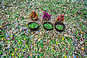 Bogura, Bangladesh - 10 August 2022: Aerial view of women amidst a sea of discarded plastic bottles, sorting through the waste with colorful clothes and baskets.
