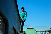 Chittagong, Bangladesh - 28 November 2019: View of a young man perched precariously on the side of a moving train, bathed in the warm sunlight.