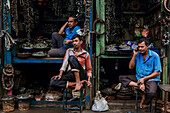 Dhaka, Bangladesh - 09 November 2019: View of three men sitting in a shop filled with metal chains and hardware, a scene of everyday commerce.