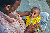 Bogura, Bangladesh - 07 October 2015: View of a tender moment as a man cradles a baby in his arms, their gazes locked in gentle affection against the backdrop of weathered steps.
