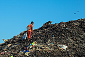Chattogram, Bangladesch - 03. November 2019: Blick auf ein Kind, das sich unter blauem Himmel durch den kahlen, geschwärzten Müllberg bewegt, mit einem Hund in der Nähe.