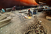Dhaka, Bangladesch - 05. November 2021: Blick auf Arbeiter, die inmitten der düsteren, sonnenüberfluteten Werft schuften und Funken sprühen, während sie riesige Schiffe reparieren - ein Zeugnis der Industrie.