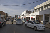 Kisumu, Kenya - 13 May 2021: View of a bustling street scene with cars and pedestrians amidst colonial-era architecture under a bright sky.