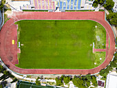 Aerial view of the vibrant green rectangle of a sports field encircled by a red running track, nestled near buildings with colorful seating, Makarska, Split-Dalmatia County, Croatia.