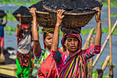 Dhaka, Bangladesh - 17 March 2017: View of women carrying heavy baskets of coal, their vibrant saris a stark contrast to the dark loads.