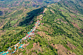 Luftaufnahme einer kurvenreichen Straße, die sich durch üppig grüne Hügel mit bunten Dächern schlängelt, Sajek Valley, Rangamati Hill District, Bangladesch.