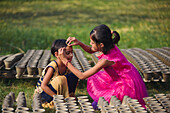 Bogura, Bangladesh - 19 November 2020: View of two young girls amidst rows of terracotta pots, one gently touching the other's forehead in a tender moment, with sunlight highlighting the textures.