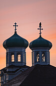View of twin, teal-domed Orthodox church spires piercing the soft, pastel-colored sky, a testament to faith and architectural beauty, Unalaska, Alaska, United States.