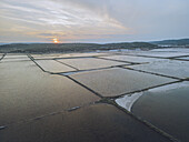 Luftaufnahme von geometrischen Salzpfannen, in denen sich der pastellfarbene Himmel nahe der Küste spiegelt, eine ruhige Szene in einem vom Menschen veränderten Feuchtgebiet, Gruissan, Okzitanien, Frankreich.
