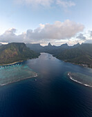 Luftaufnahme des tiefblauen Kanals im Kontrast zu den flachen türkisfarbenen Riffen, umgeben von üppig grünen Bergen, Moorea, Inseln über dem Winde, Französisch-Polynesien.