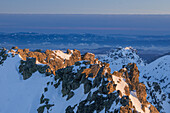 View of snow-capped peaks kissed by the warm glow of the sun, creating a striking contrast against the cold, shadowy valleys, Vysoké Tatry, Prešov Region, Slovakia.