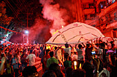 Chattogram, Bangladesch - 09. Oktober 2022: Blick auf eine Menschenmenge, die sich unter einer großen, beleuchteten Struktur inmitten eines Dunstes aus leuchtend rotem Rauch versammelt hat.