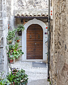 View of a rustic, wooden door framed by aged stone walls and vibrant potted plants, creating a charming and inviting scene, Pacentro, Abruzzo, Italy.