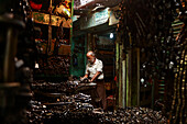 Dhaka, Bangladesh - 09 November 2019: View of an artisan meticulously working at his craft in a dimly lit workshop, surrounded by piles of metal and tools.