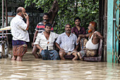 Satkania, Bangladesh - 09 August 2023: View of floodwaters engulfing the area, where resilient men gather amidst the deluge, their faces etched with worry under the overcast sky.