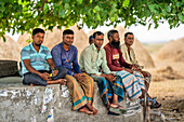 Bogura, Bangladesh - 12 May 2024: View of men seated by stacked haystacks, their varied attire contrasting against the rural landscape.