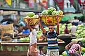 Dhaka, Bangladesh - 09 April 2022: View of men carrying baskets of watermelons in the bustling market, a vibrant scene of labor and trade.