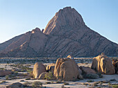 Luftaufnahme der Spizklopp-Felsformation mit einem Mann, der auf einem Felsen in einer weiten, trockenen Landschaft steht, Erongo, Namibia.