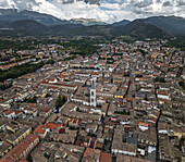 Luftaufnahme von Terrakotta-Dächern und sonnenbeschienenen Fassaden, die sich über den antiken Stadtteppich ergießen, der durch den hoch aufragenden Glockenturm des Annunziata-Komplexes verankert ist, Sulmona, Provinz L'Aquila, Italien.