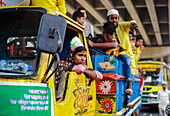 Chattogram, Bangladesh - 21 November 2018: View of people riding atop a brightly painted yellow truck, a vibrant spectacle against the urban backdrop.