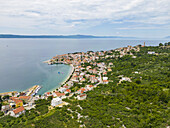 Luftaufnahme von Terrakotta-Dächern, die kaskadenförmig in die türkisfarbene Adria abfallen, umrahmt von grünen Hügeln, Igrane, Gespanschaft Split-Dalmatien, Kroatien.