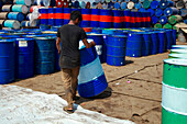 Narayanganj, Bangladesh - 27 February 2021: View of a worker amidst a sea of blue and red metal drums, creating a strong contrast against the sandy ground.