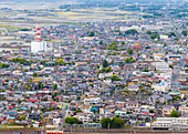 Luftaufnahme von dicht gedrängten Häusern, die von einem rot-weißen Turm und grünen Flecken unterbrochen werden - ein weitläufiges Stadtbild entfaltet sich, Chikusei, Ibaraki, Japan.