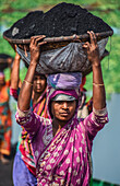 Dhaka, Bangladesh - 17 March 2017: View of women carrying baskets of dark coal on their heads, their vibrant pink and red saris a stark contrast to the dark load..