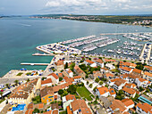 Luftaufnahme von Gebäuden mit roten Dächern, eingebettet zwischen den strahlend weißen Yachten des Jachthafens unter einem weiten Himmel, dahinter die Adria, Biograd na Moru, Gespanschaft Zadar, Kroatien.