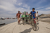 Chittagong, Bangladesh - 09 September 2022: View of men pushing a cart along the ghat, the sun reflecting off the water and concrete.