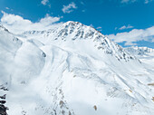 Aerial view of the majestic, snow-laden peaks piercing a crisp blue sky, contrasting textures of ice and rock under the sun, Altai Mountains, Bayan-Ölgii, Mongolia.