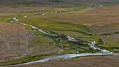 Blick auf einen sich schlängelnden Fluss, der sich durch die weiten Deosai-Ebenen schlängelt, ein Wandteppich aus Braun- und Grüntönen unter dem weiten Himmel, Deosai-Nationalpark, Gilgit Baltistan, Pakistan.