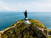 Luftaufnahme der Cristo Rei-Statue, die hoch oben auf einem üppigen, grünen Hügel steht und das ruhige, tiefblaue Meer überblickt, Dili, D?li, Timor-Leste.