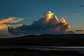 View of a golden-lit cloud formation over a dark landscape and a winding river, reflecting the last light of day, Deosai National Park, Gilgit Baltistan, Pakistan.