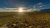 View of the sun shining bright over the green grasslands with a small river running through, under a blue sky with fluffy clouds, Skardu, Gilgit Baltistan, Pakistan.
