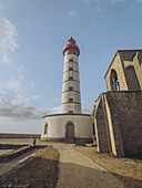 View of the Phare de Saint-Mathieu lighthouse rising majestically against the blue sky, a serene beacon next to ancient stone ruins, Plougonvelin, Bretagne, France.