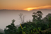 View of the golden sun dips behind distant mountains, casting a warm glow over the lush green forest below, painting the sky with hues of orange, Sajek, Chittagong Division, Bangladesh.